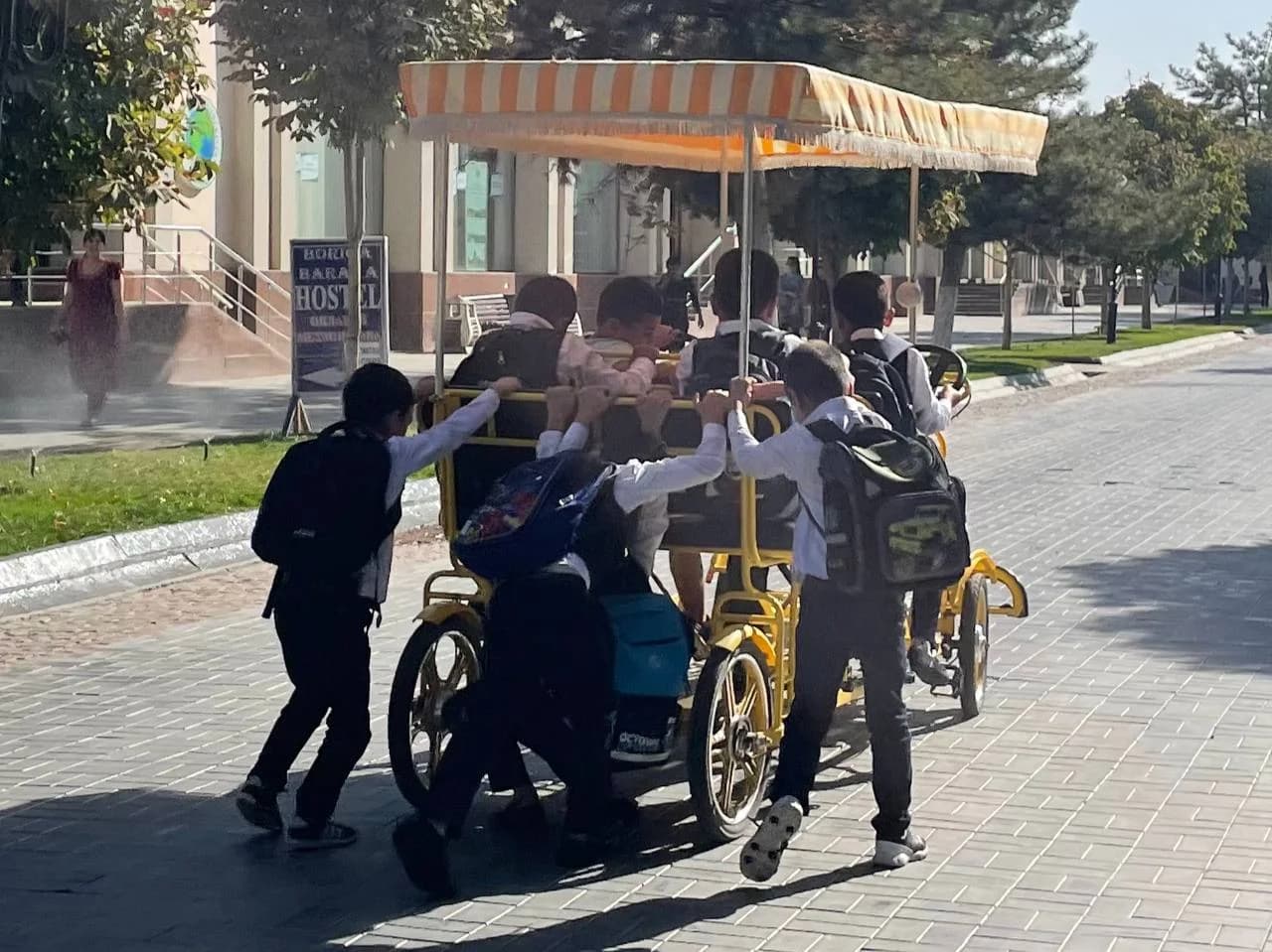 Maktab kiyimidagi o'quvchilar ko'p o'rinli velosipedni orqasidan itarib ketishmoqda