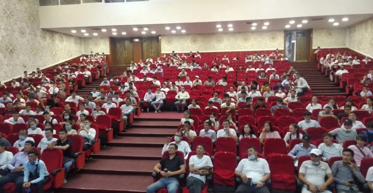 Teatr zalidagi qizil o'rindiqlarda o'tirgan ko'p sonli tomoshabinlar