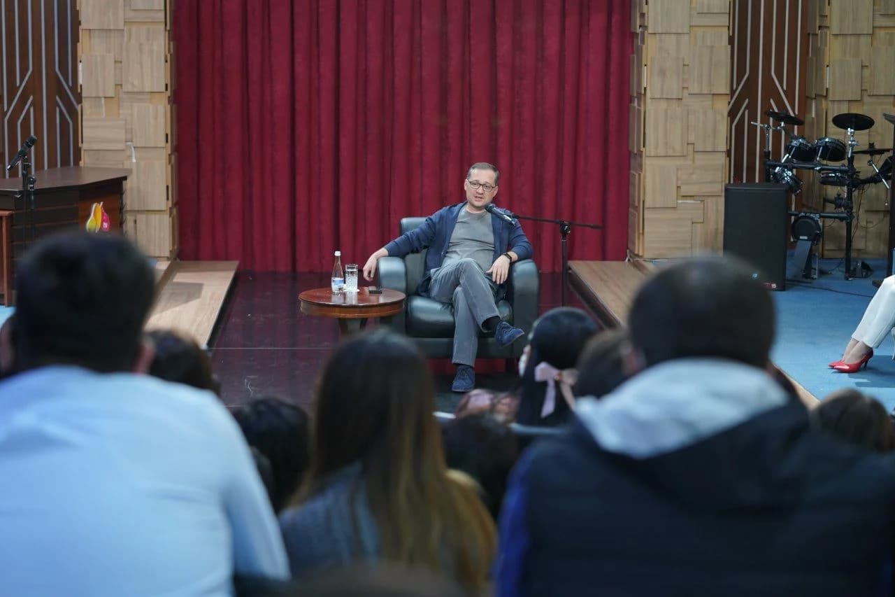 Komil Allamjonov studiya markazidagi kresloda uchrashuv ishtirokchilari bilan muloqot qilmoqda