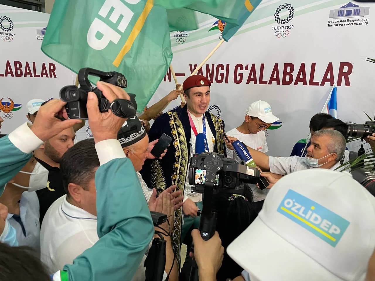 Chopon kiygan va medal taqqan sportchi jurnalistlarga intervyu bermoqda