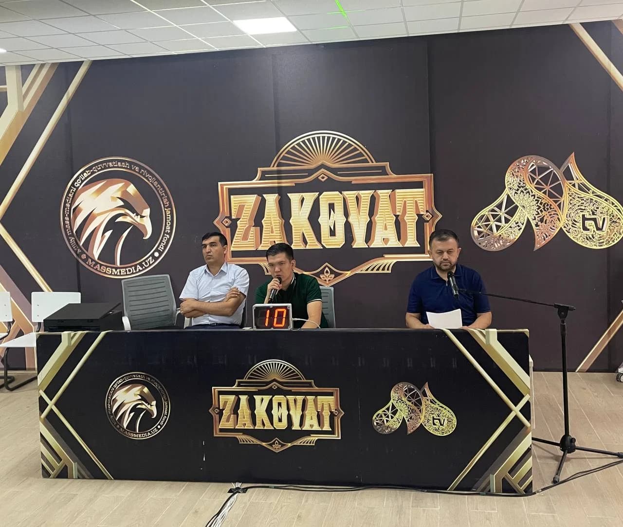 Zakovat logotipi tushirilgan minbar ortida o'tirgan hakamlar va tashkilotchilar